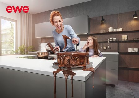 Mutter und Tochter beim Schokotorte-verzieren in grauer Küche, alles tropft