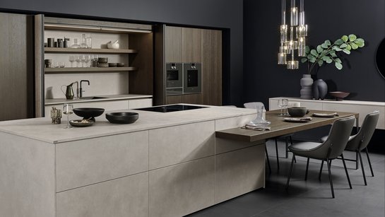 Kücheninsel in Betonoptik mit angesetzter Bar und Esstisch in dunklem Holz