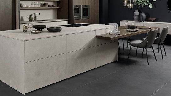 Kücheninsel in Betonoptik mit angesetzter Bar und Esstisch in dunklem Holz