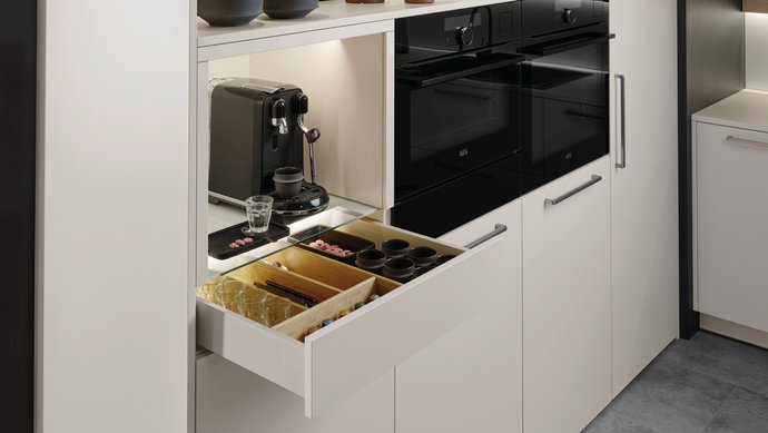 Helle Hochschrankgruppe mit einer Nische für Kaffeemaschinen, die Lade darunter für Kaffeezubehör ist geöffnet