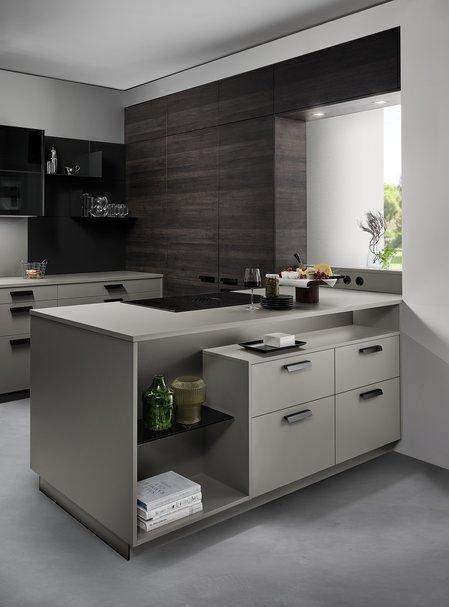 ewe Nuova/Unita in fossil/eiche ganache Graue Kücheninsel mit eingebauter Nische, dahinter eine Rückwand in dunkler Holzoptik mit versteckter Tür