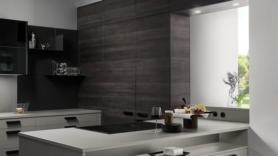 Graue Kücheninsel mit eingebauter Nische, dahinter eine Rückwand in dunkler Holzoptik mit versteckter Tür