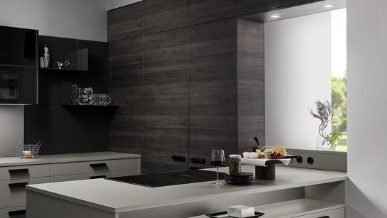 Graue Kücheninsel mit eingebauter Nische, dahinter eine Rückwand in dunkler Holzoptik mit versteckter Tür