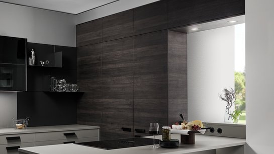 Graue Kücheninsel mit eingebauter Nische, dahinter eine Rückwand in dunkler Holzoptik mit versteckter Tür