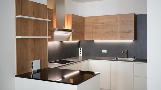 In kleinen Raum eingebaute U-förmige Küche in weiß mit dunkler Arbeitsplatte und holzfarbenen Oberschränken