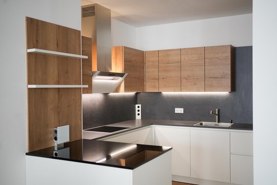 In kleinen Raum eingebaute U-förmige Küche in weiß mit dunkler Arbeitsplatte und holzfarbenen Oberschränken