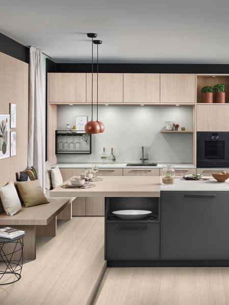 ewe Colora/Nordic in cameroon/eiche weiß nordic Große dunkle Kücheninsel vor einer Küchenzeile aus hellem Holz, links an der Insel ist eine Sitzbank