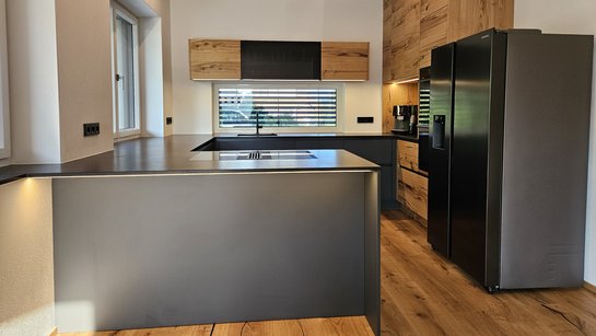 Dunkelgraue Küche in U-Form, kombiniert dazu Hoch- und Oberschränke aus Risseiche