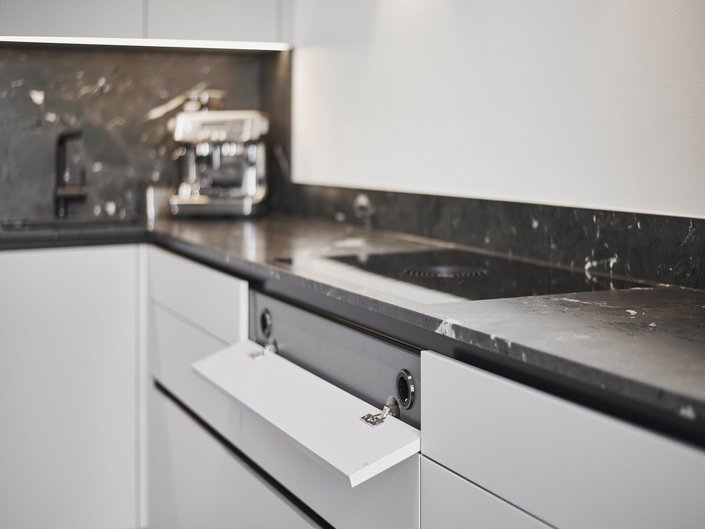 Clever gelöst: Steckdosen verstecken sich dezent hinter einer abklappbaren Front unter dem Kochfeld.