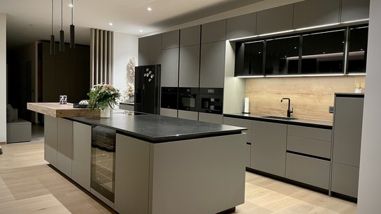Graue Inselküche mit schwarzer Arbeitsplatte und beleuchteten dunklen Glasoberschränken