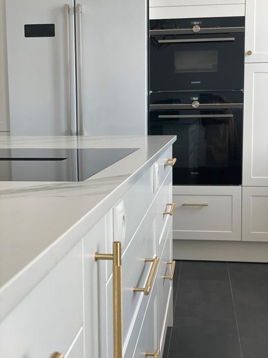 Ausschnitt einer Kücheninsel mit weißen Landhausfronten, goldenen Griffen und einer Kochplatte