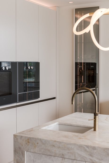 Hochschrankwand mit integrierten Elektrogeräten und beleuchtetem Glasvitrinenschrank.