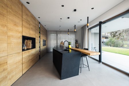 ewe Sintesa/Nuova in eiche umbria/schwarz | Elektro Müller, Landeck Schwarze Kücheinsel mit Barplatte aus Holz, dahinter deckenhoch verbaute Hochschränke in eiche umbria