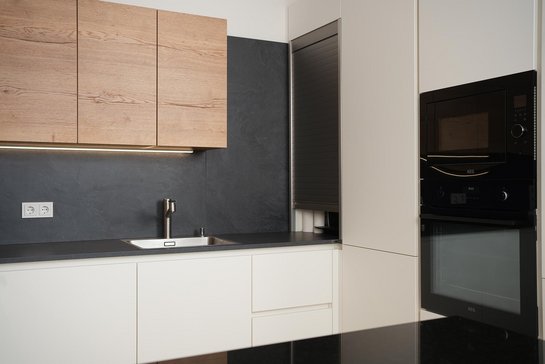 In kleinen Raum eingebaute U-förmige Küche in weiß mit dunkler Arbeitsplatte und holzfarbenen Oberschränken