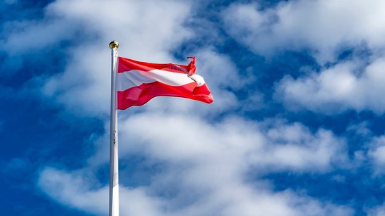 Eine österreichische Flagge weht vor einem blauen Himmel mit Wolken