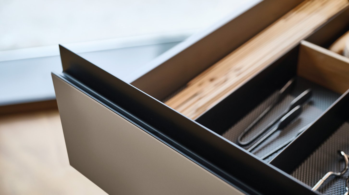 ewe GL30 in schwarz eloxiert gezeigt an ewe nanoo® . ewe Nordic in lehmbraun . eiche dunkel nordic, 18er Raster Schublade mit schwarzer Gl30 Griffleiste und Inneneinteilung.