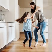 Eine Mutter und ihre kleine Tochter tanzen gemeinsam in einer weißen Küche