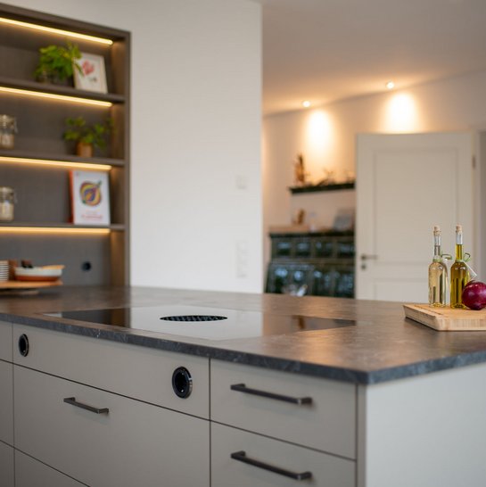 Moderne Kücheninsel in lehmbraun mit schwarzen Griffen und einem in der Wand eingebauten offenen Regal