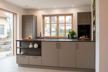 Moderne Kücheninsel in lehmbraun mit eingebauter Nische, dahinter eine Küchenzeile im Landhausstil in steineiche furniert