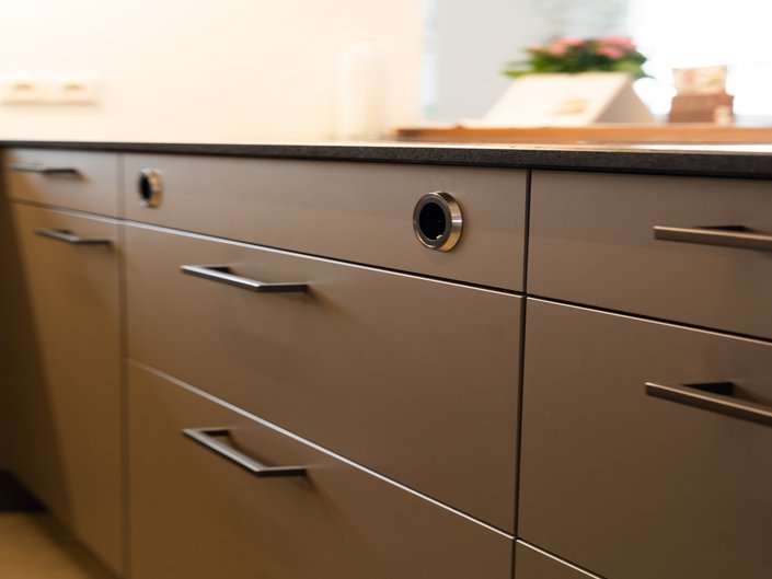 Ausschnitt der Front einer grauen Kücheninsel mit schwarzen Griffen und Steckdosen