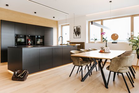 Links im Bild eine Inselküche in anthrazit, rechts eine helle, moderne Esstischgruppe