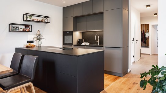 Inselküche mit schwarzer Inselküche und grauer Hochschrankgruppe dahinter
