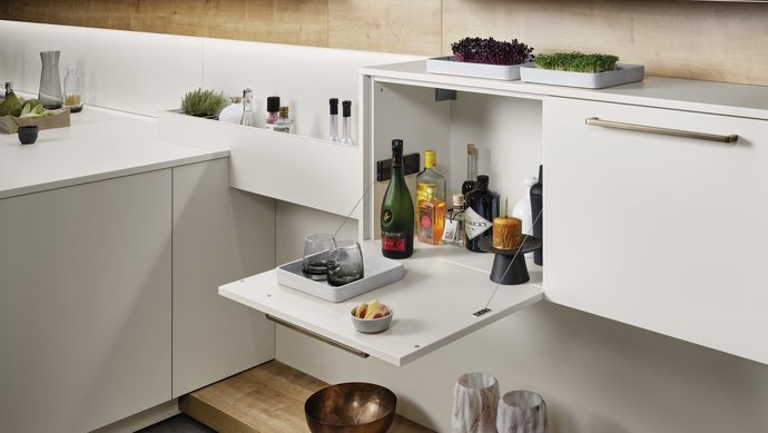 Ein an der Wand montiertes Sideboard, in dem ein Regal nach unten geklappt geöffnet ist und als Bar dient