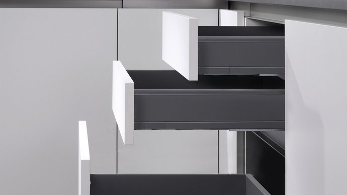 Seitliche Aufnahme eines Unterschranks mit drei geöffneten Schubladen mit grauen Wänden