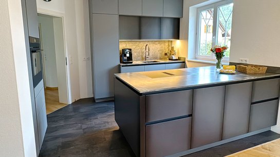 Kücheninsel in Schwarzblech-Optik, dahinter Oberschränke in grau