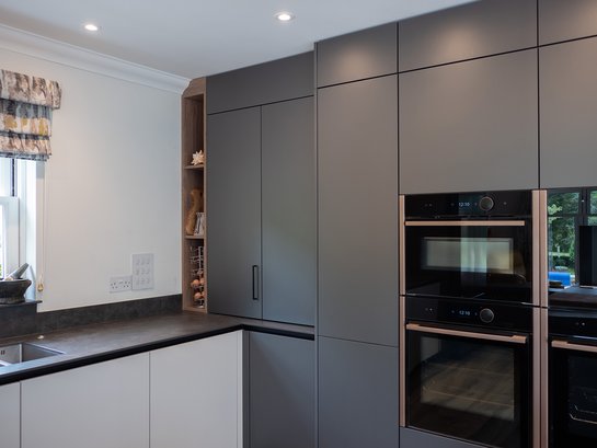 Moderne graue Küche mit hochgestellt eingebauten Elektrogeräten.