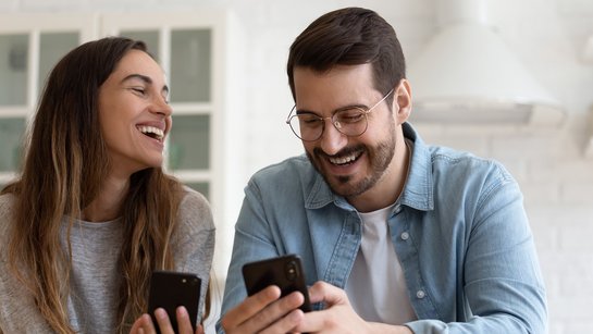 Ein Pärchen lächelt sich an, beide haben ein Smartphone in der Hand