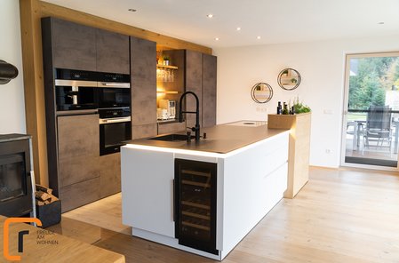 Eine weiße Kücheninsel mit schwarzer Arbeitsplatte, dahinter eine Küchenzeile in Betonoptik