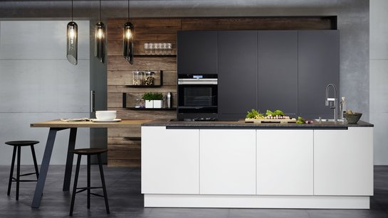 Weiße Inselküche mit angebautem Tisch mit Hockern, dahinter Hochschränke in anthrazit