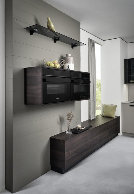 Hängeschrank mit Elektrogeräten darin, darunter ein Sideboard in dunkler Holzoptik an einer grauen Wand