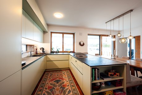 Blick in die U-Küche mit Natursteinarbeitsplatte, integrierter Spüle am Fenster und funktionaler Raumaufteilung für kurze Wege im Alltag.