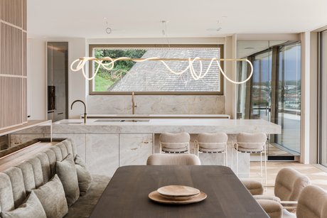 Wohnküche mit Esstisch im Vordergrund, großzügiger Insel mit Barhockern und harmonisch abgestimmten Materialien.