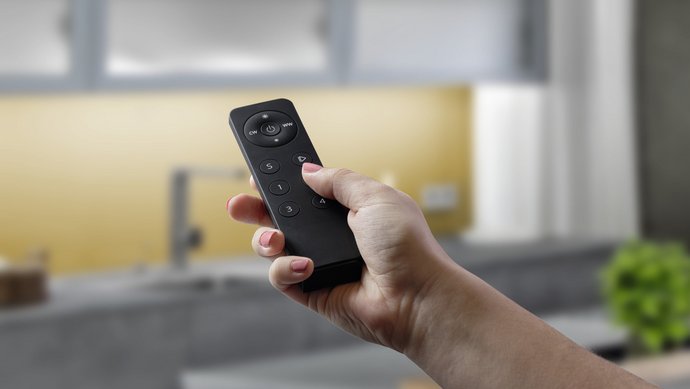 Eine Hand hält eine Fernbedienung, die die Küchenbeleuchtung einschaltet.