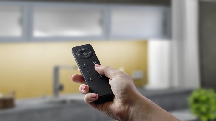 Eine Hand hält eine Fernbedienung, die die Küchenbeleuchtung einschaltet.