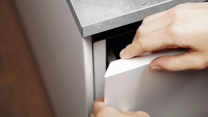Zwei Hände umfassen eine halb geöffnete Schranktür an einer Kücheninsel