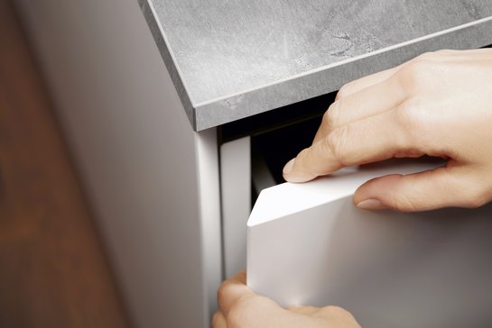 Zwei Hände umfassen eine halb geöffnete Schranktür an einer Kücheninsel