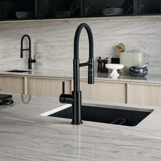 Helle Steinarbeitsplatte mit dunkler Spüle und Armatur, dahinter Glas-Oberschränke