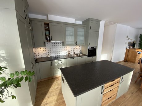Landhausküche mit Rahmenfronten in salbei, aufgebaut als Inselküche mit schwarzer Arbeitsplatte