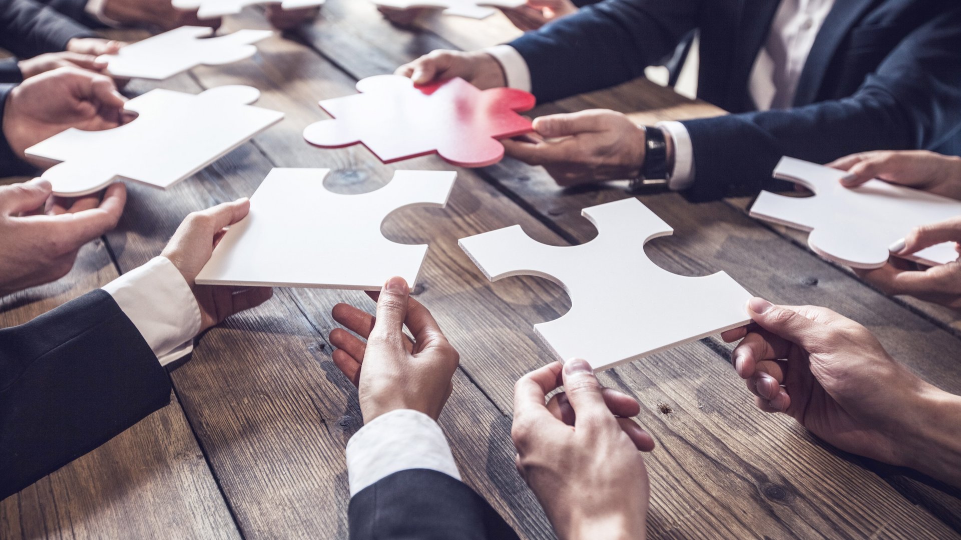 ewe Business Fachhändler Informationen Anzuggekleidete Arme halten rund um einen Tisch Puzzleteile zusammen