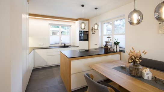 Weiße Inselküche mit Holzelementen und angebautem Esstisch