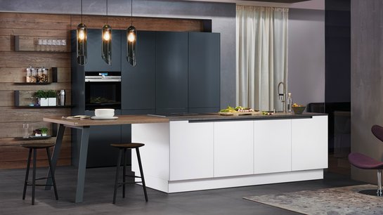 Weiße Inselküche mit angebautem Tisch mit Hockern, dahinter Hochschränke in anthrazit
