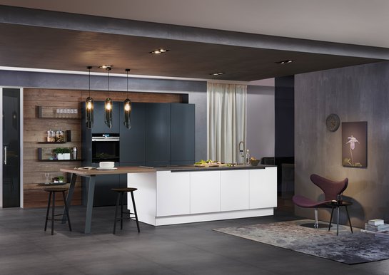 Weiße Inselküche mit angebautem Tisch mit Hockern, dahinter Hochschränke in anthrazit