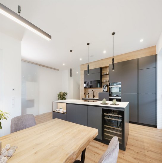 Esstisch aus hellem Holz, dahinter eine dunkelgraue Inselküche