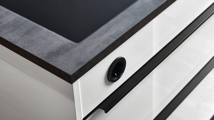 Ecke einer weißen Hochglanz-Kücheninsel mit schwarzen Griffleisten und dunkler Arbeitsplatte