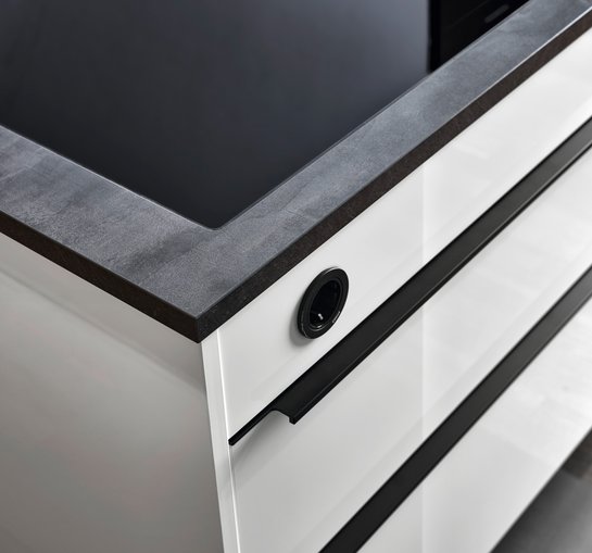 Ecke einer weißen Hochglanz-Kücheninsel mit schwarzen Griffleisten und dunkler Arbeitsplatte