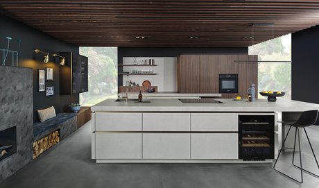 Kücheninsel mit grauer Strukturoberfläche und eingebautem Weinkühlschrank, dahinter Hochschränke in Nuss-Optik